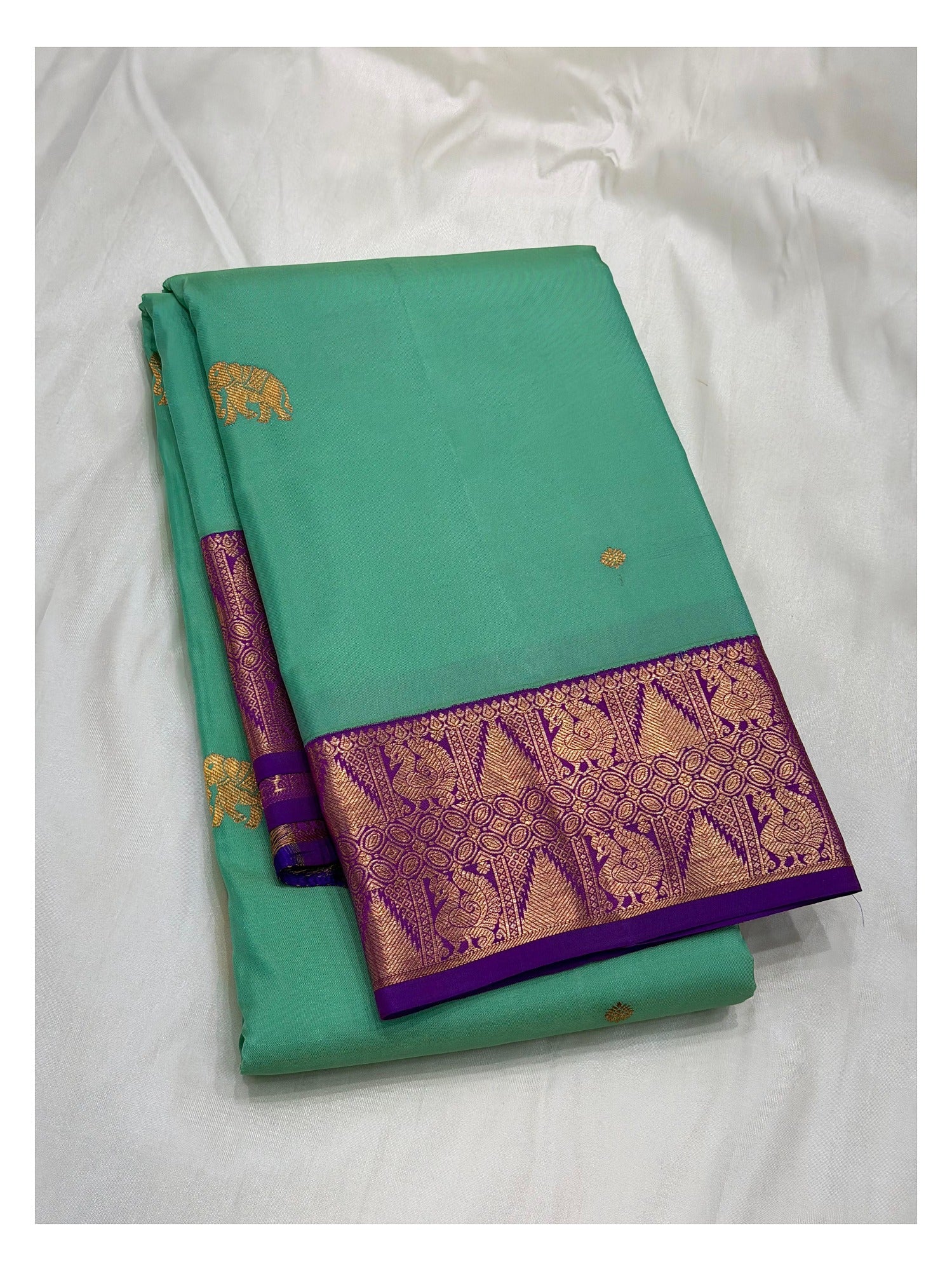 Folded aqua green handwoven Kanchipuram silk saree with purple contrast border and gold-toned woven motifs