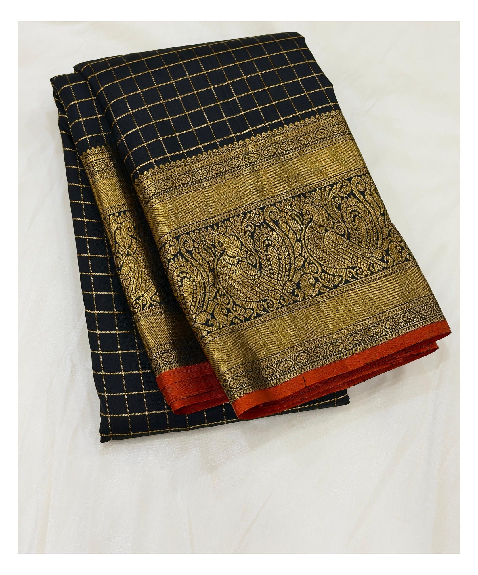 Handwoven Kanchipuram silk saree folded, showing black checked body and ornate gold-toned peacock border