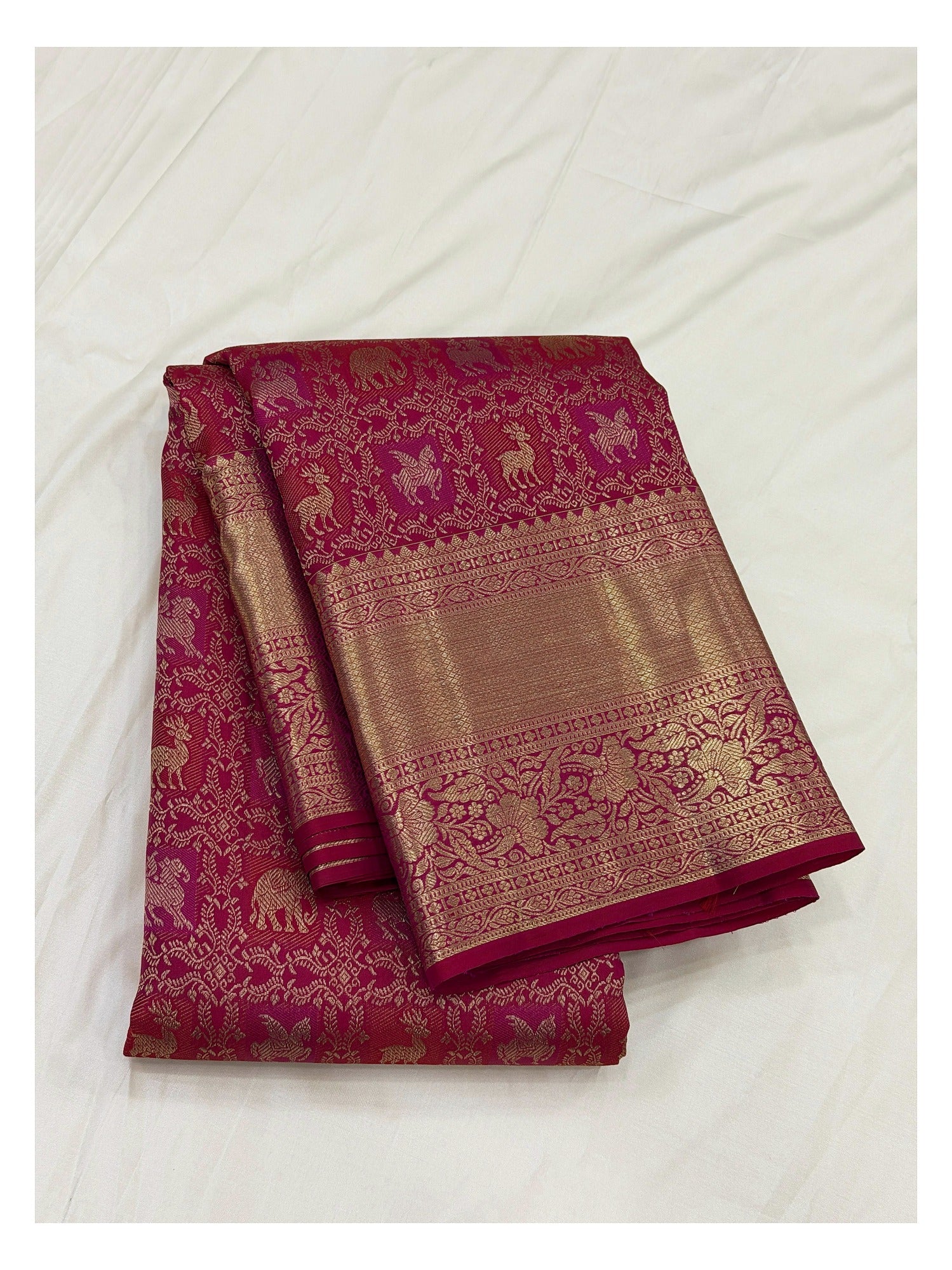 Folded deep magenta handwoven Kanchipuram silk saree with gold-toned woven motifs and broad floral border