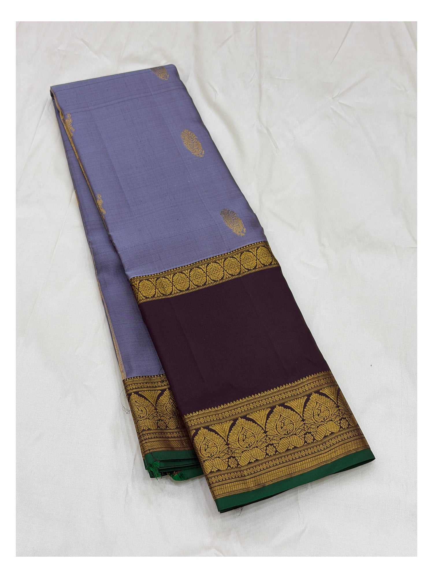 Folded lavender saree showing gold woven body motifs, deep plum border, and green edge