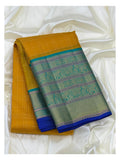 Folded mustard pure silk saree with teal woven border and royal blue edge on a white draped backdrop