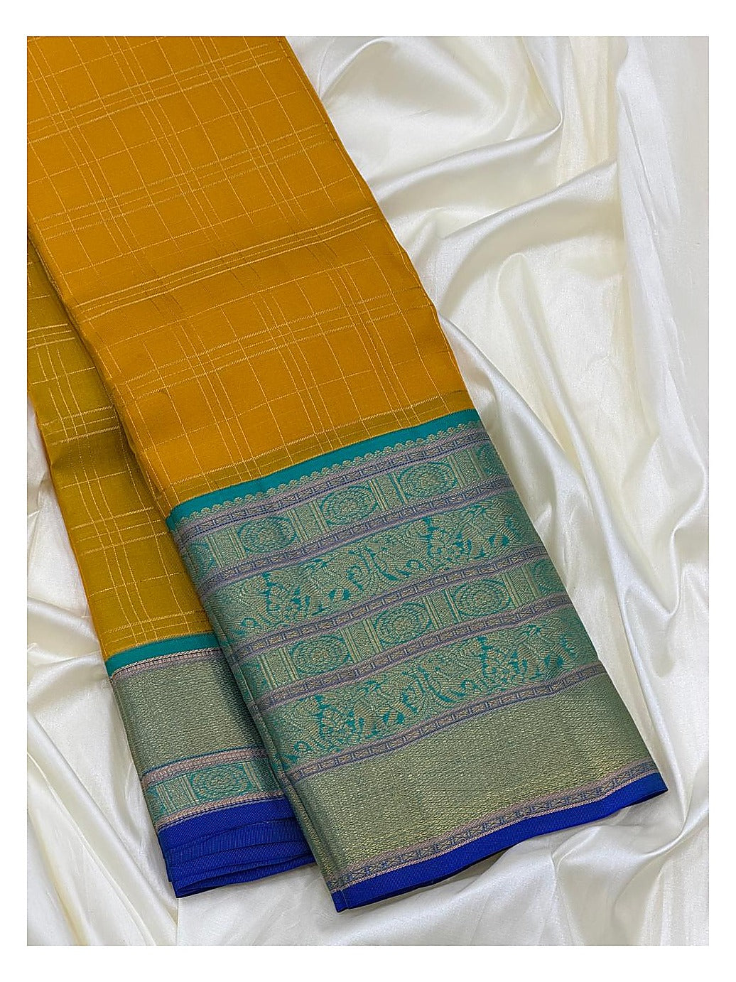 Folded mustard saree showing fine check lines and a detailed teal woven border
